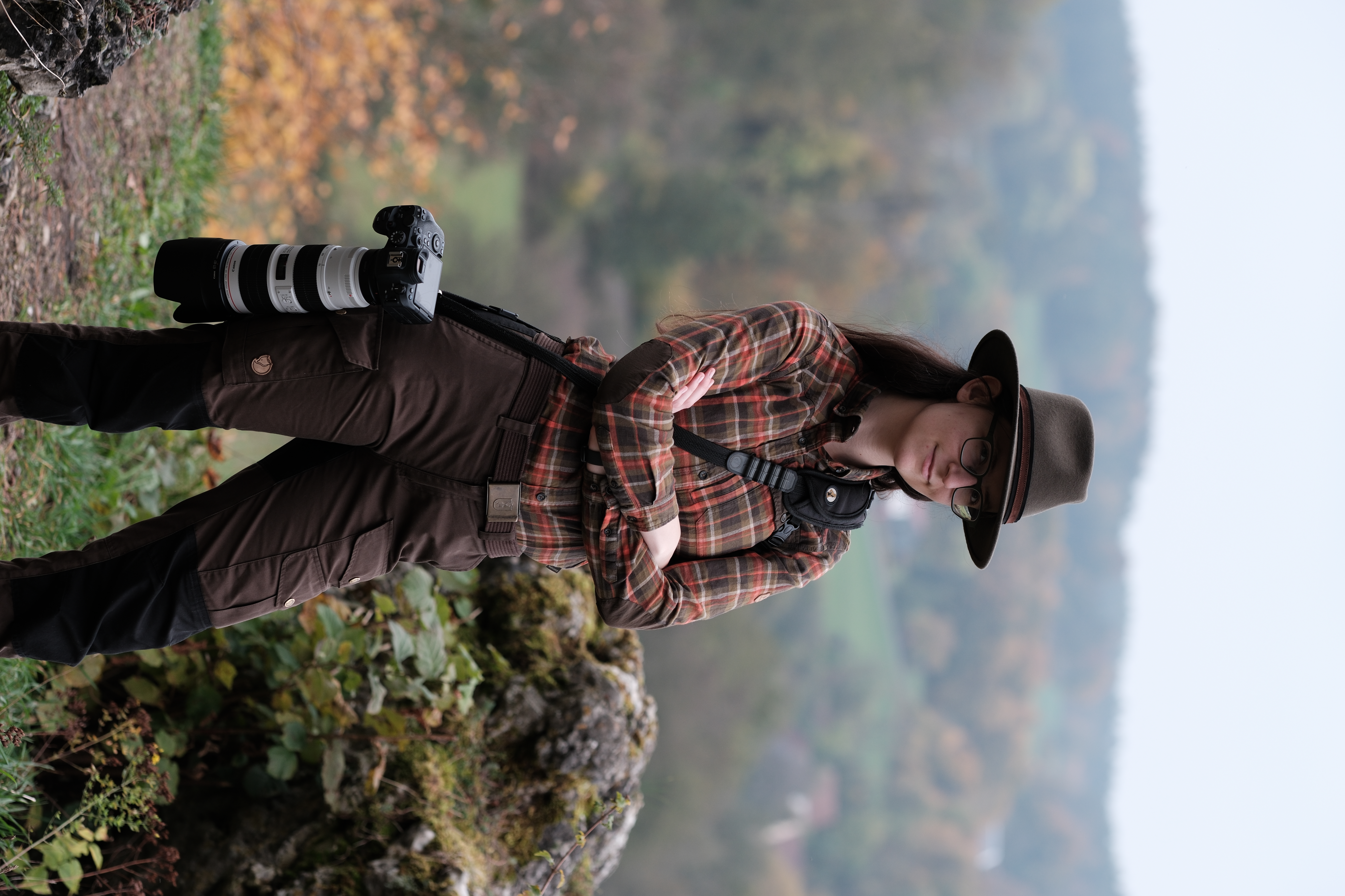 Bild einer Frau in Jagdkleidung mit Kamera an der Seite hängend vor Bergpanorama mit verkratzten Armen